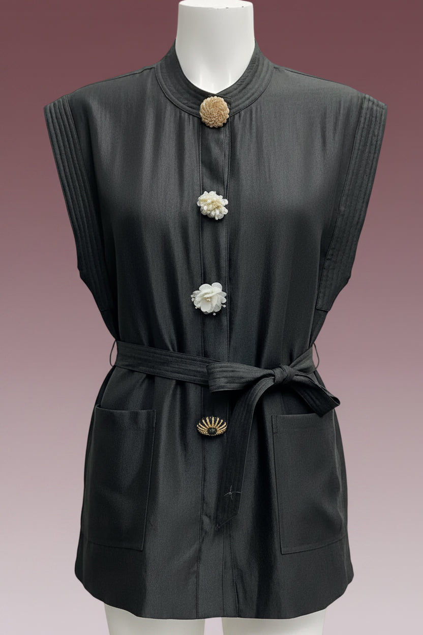 A sleeveless black linen tunic top with a high collar, decorative flower-shaped buttons, a matching fabric tie belt