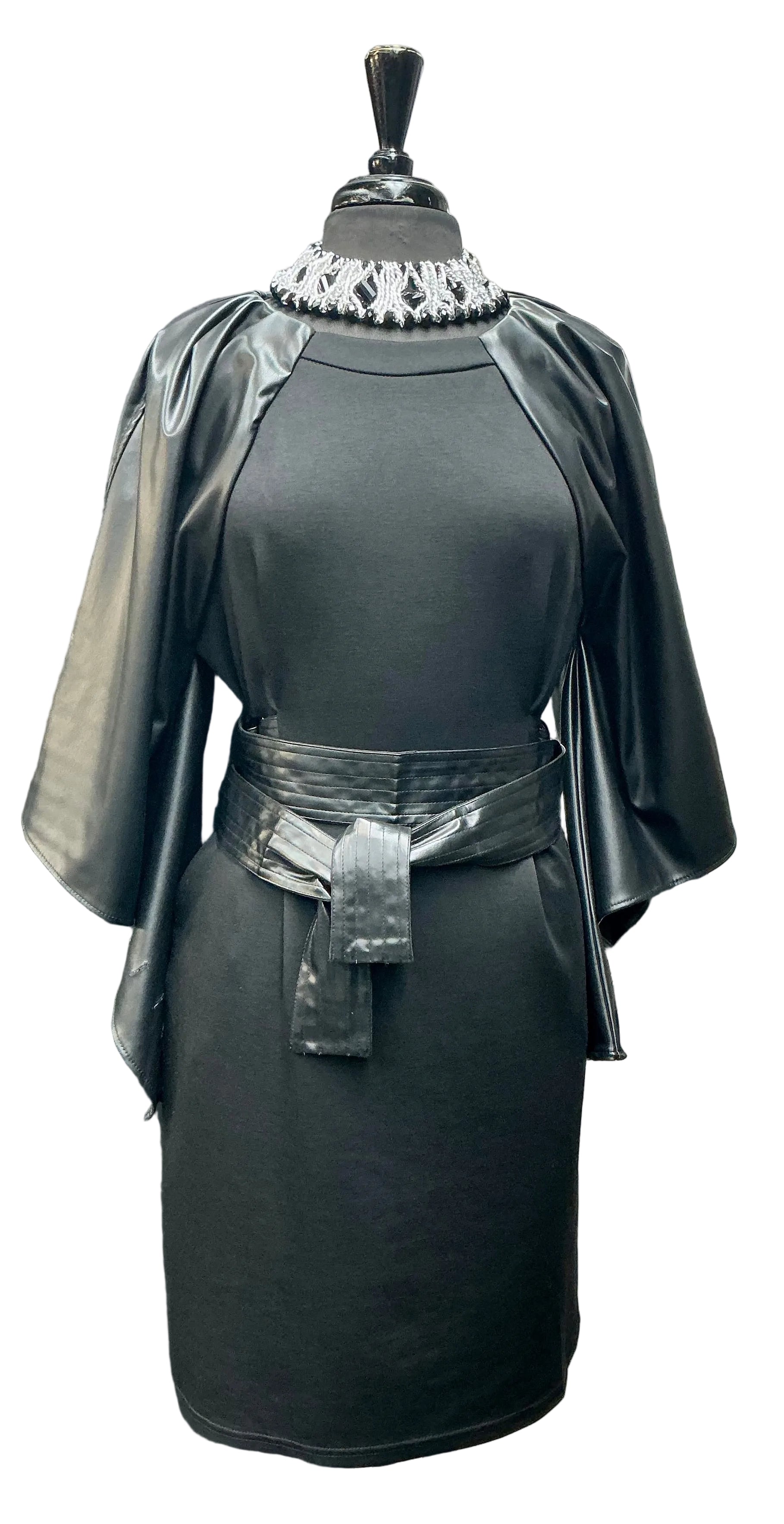 Black dress with flowing vegan leather sleeves and belt on a mannequin against a gray wall.